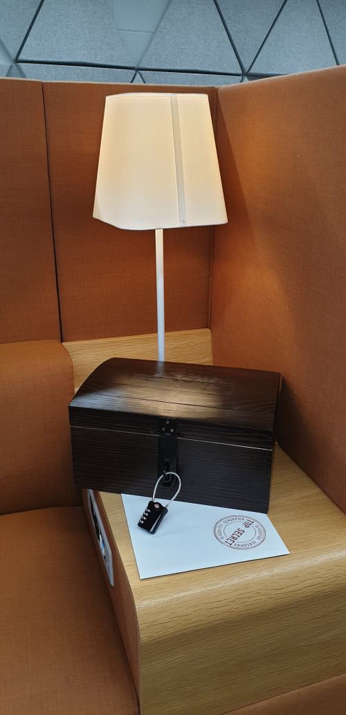 Picture shows a wooden box, fastened with a combination lock. It is sitting on top of a top secret envelope.